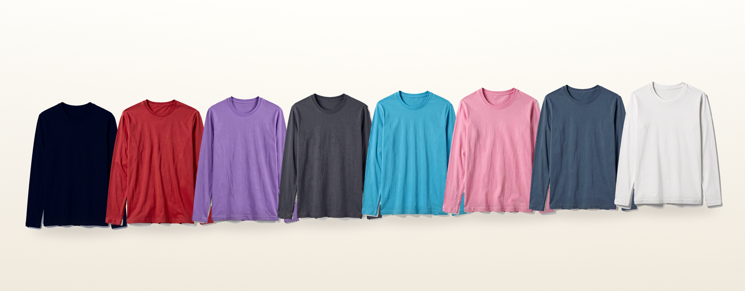 Eight plain long-sleeve crew-neck tees in eight colors, lined up in one row on a warm white background